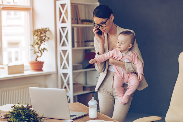 a mother talking on phone holding baby reaching for her computer