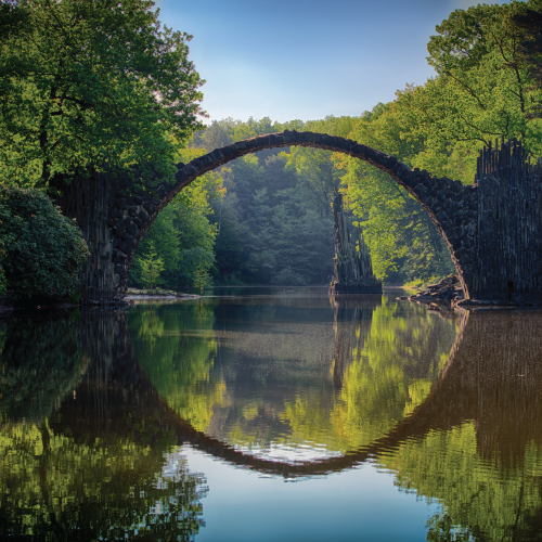a stone arched bridge across water surrounded by trees