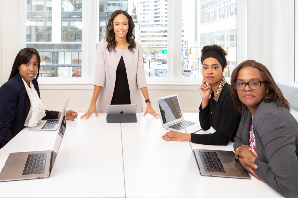three women sitting at laptops and one woman standing behind a laptop all looking at the camera with confident expressions