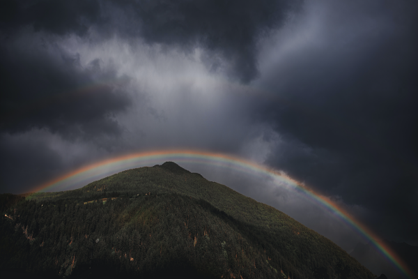 a mountain under a dark sky with a rainbow above it