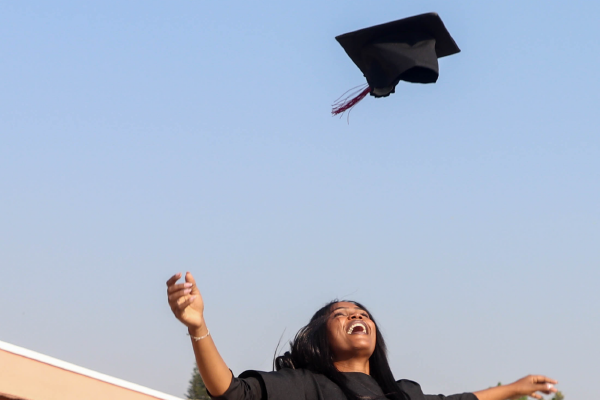 a smiling person throwing their graduation cap in the air against a cloudless sky