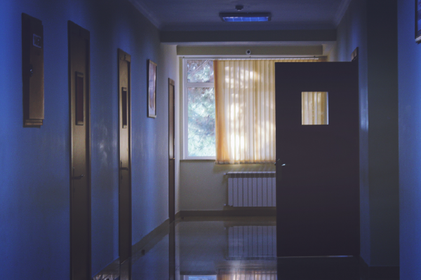 a dark hallway with one open door and a sunlit window at the end