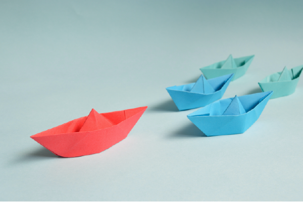 a photo of a red paper boat leading three blue paper boats
