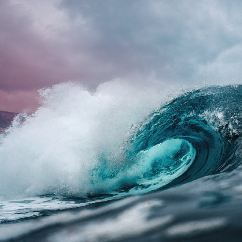 a crashing wave with a dark pink and purple sky in the background