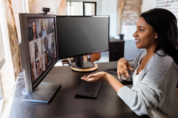 an image of a person seated in front of two computer monitors, speaking over video conference on one