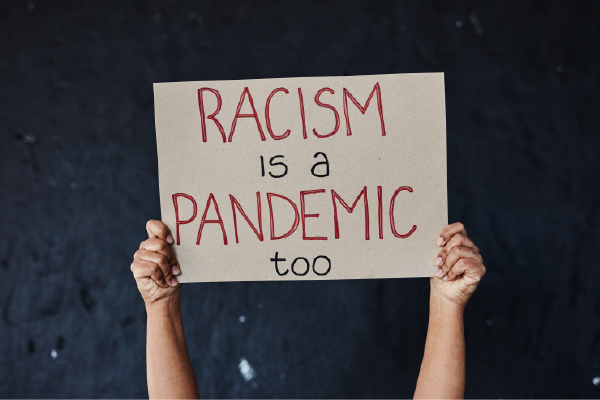 a person's hands holding up a sign that says "racism is a pandemic too"