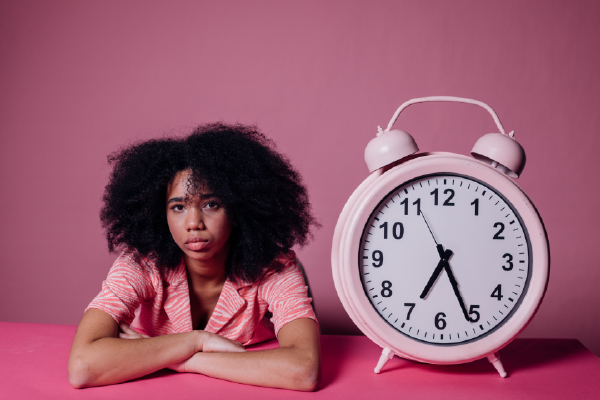 an image of a person looking frustrated next to a oversized pink clock with a pink background