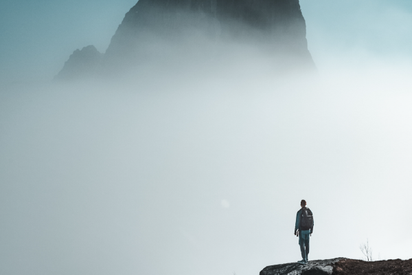 an image of a person looking into the fog with a rock formation appearing behind