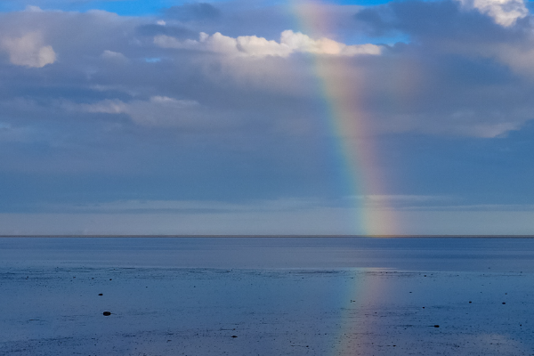 an image of a rainbow reflected in a large body of water with a partially cloudy sky