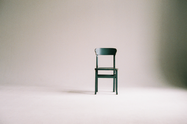 an image of an empty wooden chair against a beige wall on a beige floor