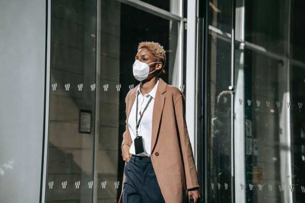 an image of a person walking in front of an office building, wearing a face mask and carrying a briefcase